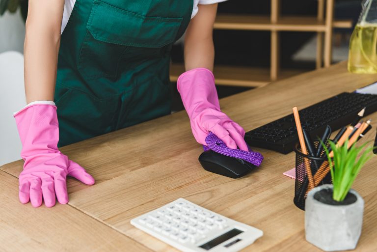 cropped shot of woman in rubber gloves cleaning office table